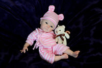 Thumbnail for A baby doll wearing a pink and white striped outfit, showcasing a cute smile and round cheeks.