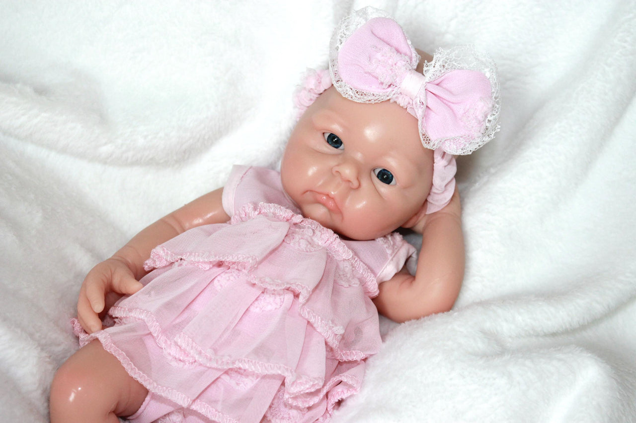 A baby doll in a pink dress and headband, showcasing a cheerful expression and delicate features.