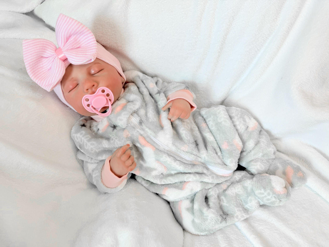 Newborn baby girl in a gray outfit with a pink bow, peacefully resting on a soft blanket.