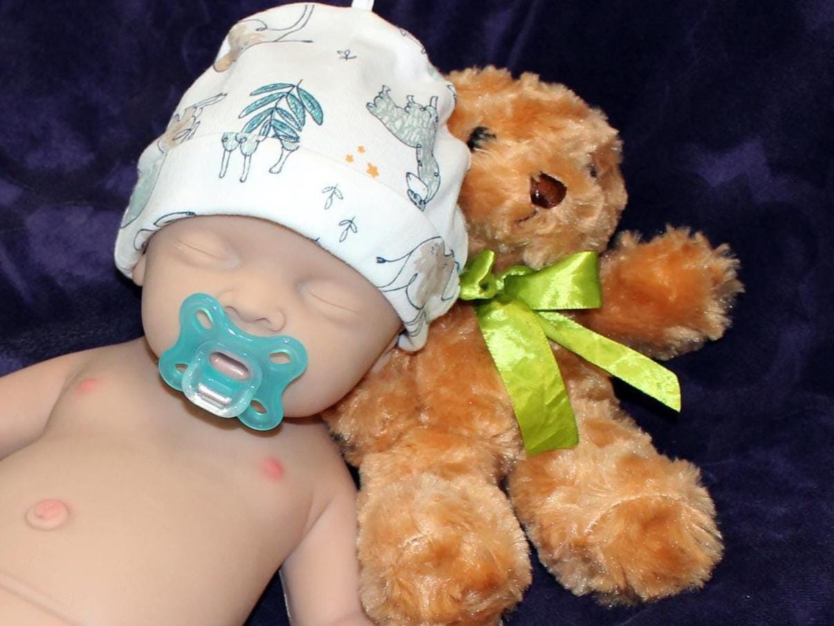 A baby doll rests on a soft purple blanket beside a cuddly teddy bear, creating a serene and playful scene.