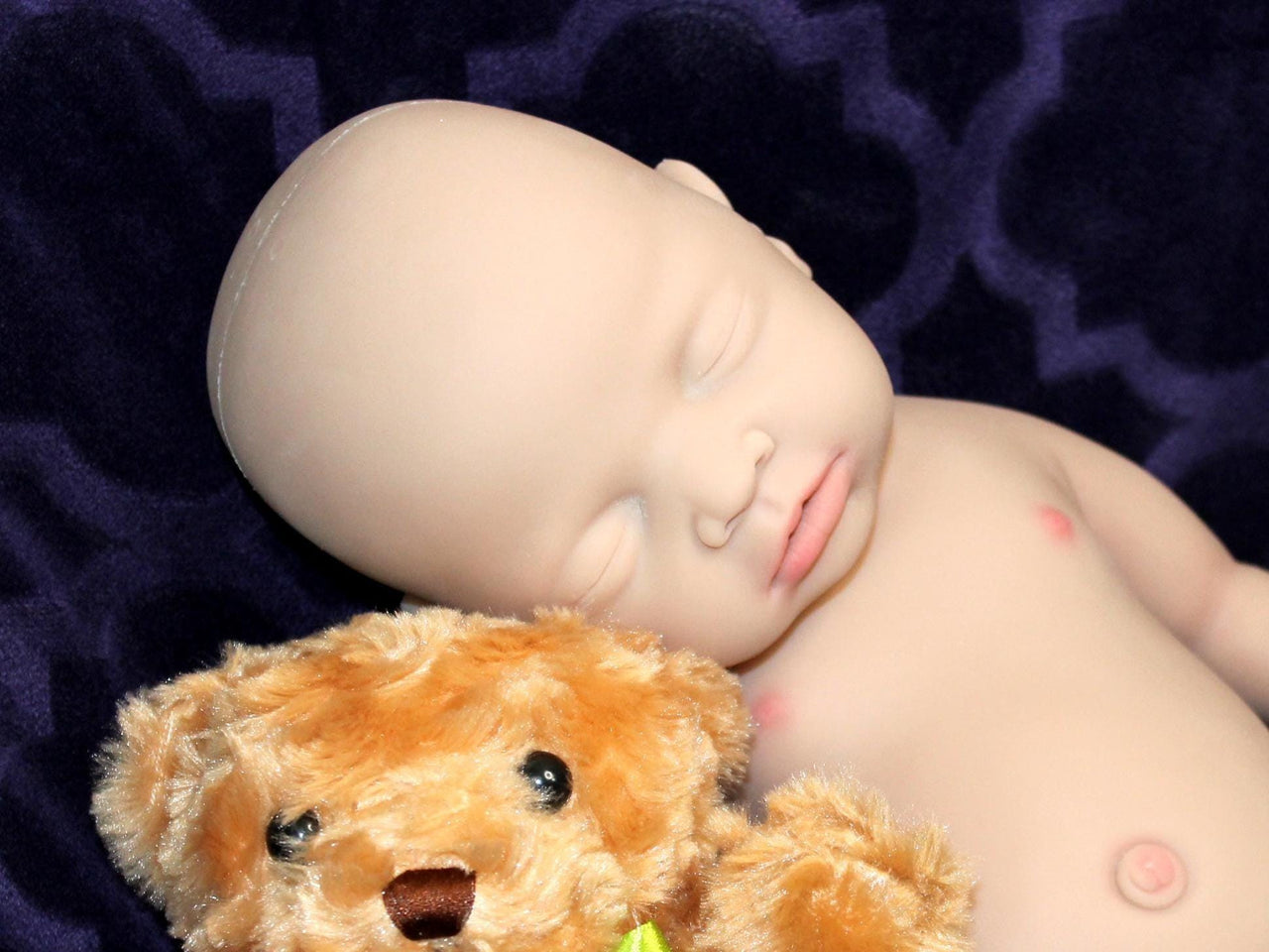 Full Silicone Doll baby doll rests on a soft purple blanket beside a cuddly teddy bear, creating a serene and playful scene.