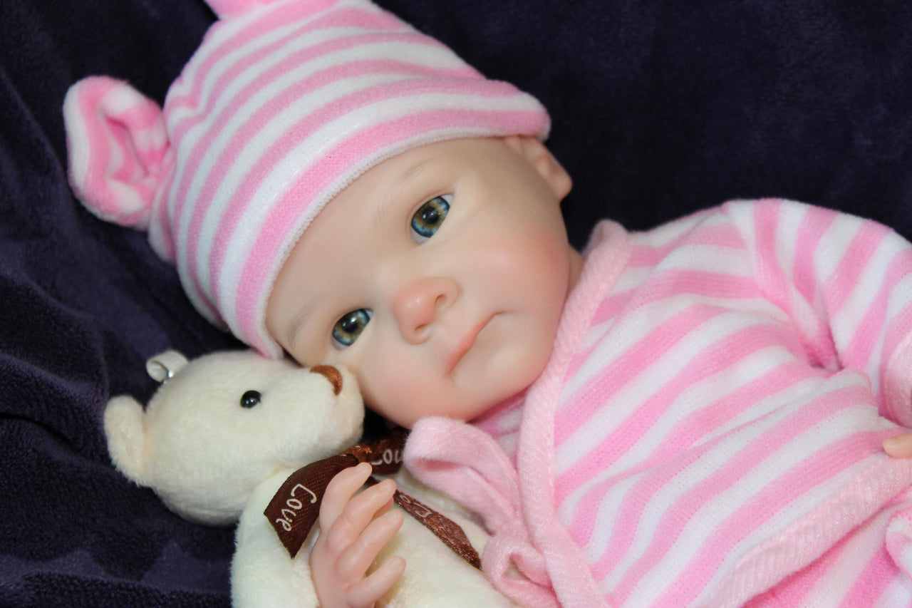 A baby doll wearing a pink and white striped outfit, showcasing a cute smile and round cheeks.