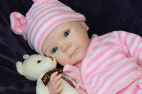 Thumbnail for A baby doll wearing a pink and white striped outfit, showcasing a cute smile and round cheeks.