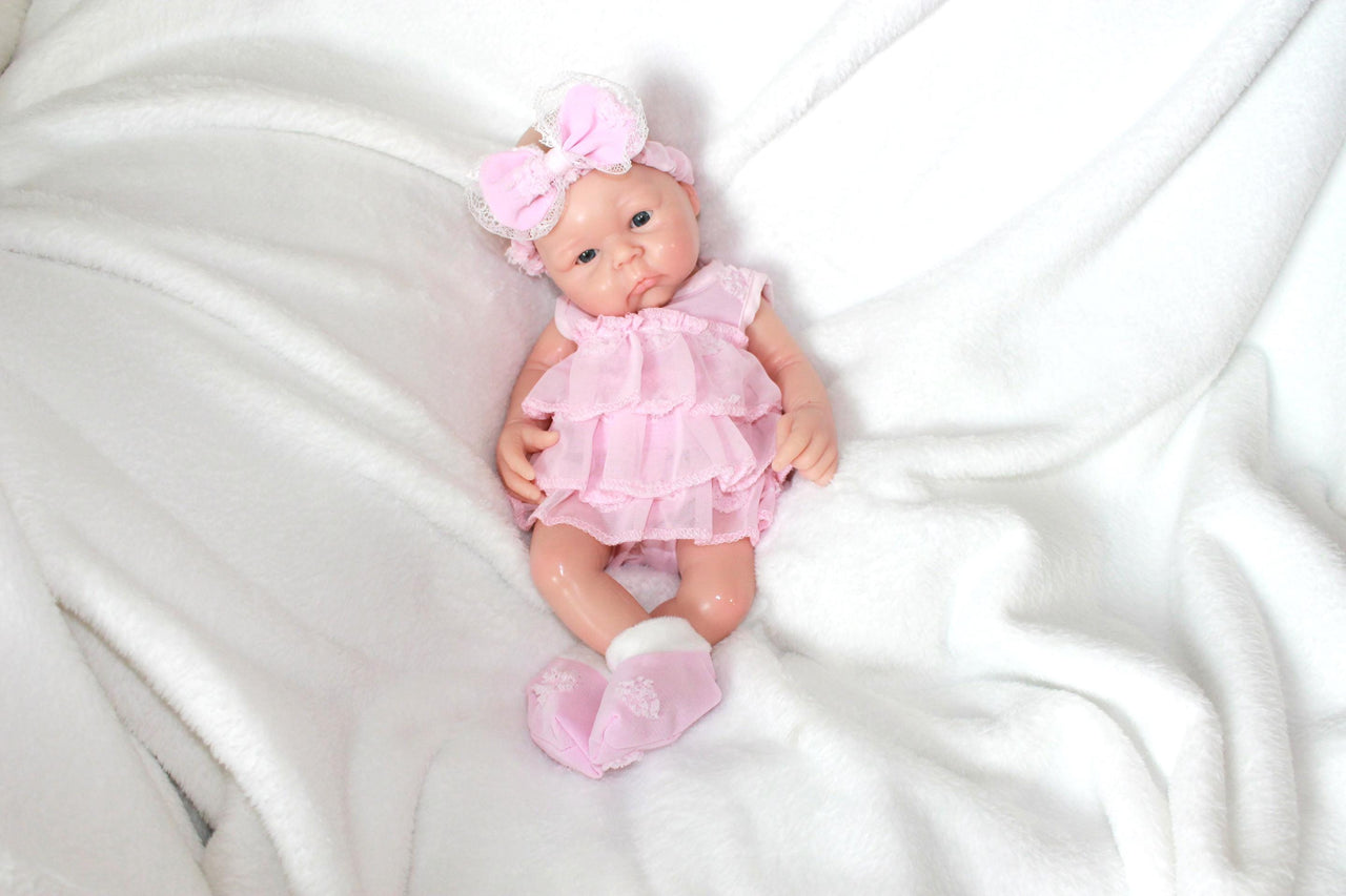 A baby doll in a pink dress and headband, showcasing a cheerful expression and delicate features.