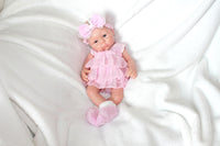 Thumbnail for A baby doll in a pink dress and headband, showcasing a cheerful expression and delicate features.
