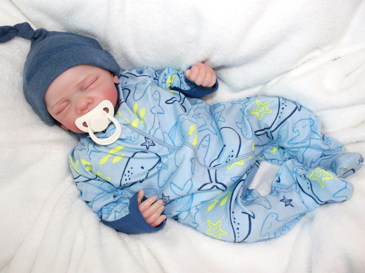 A baby doll resting on a soft blanket, showcasing its delicate features and clothing.