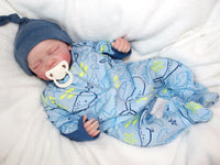 Thumbnail for A baby doll resting on a soft blanket, showcasing its delicate features and clothing.