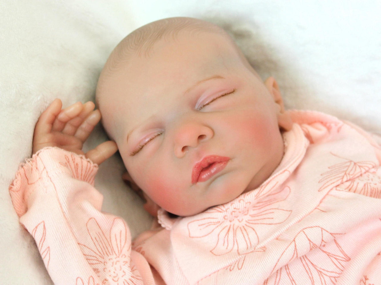 A peaceful newborn baby sleeps soundly in a soft pink outfit, surrounded by a cozy blanket.