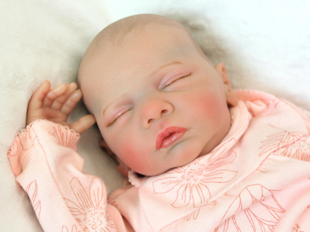 A peaceful newborn baby sleeps soundly in a soft pink outfit, surrounded by a cozy blanket.