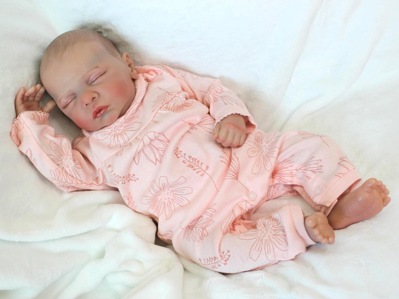 A peaceful newborn baby sleeps soundly in a soft pink outfit, surrounded by a cozy blanket.