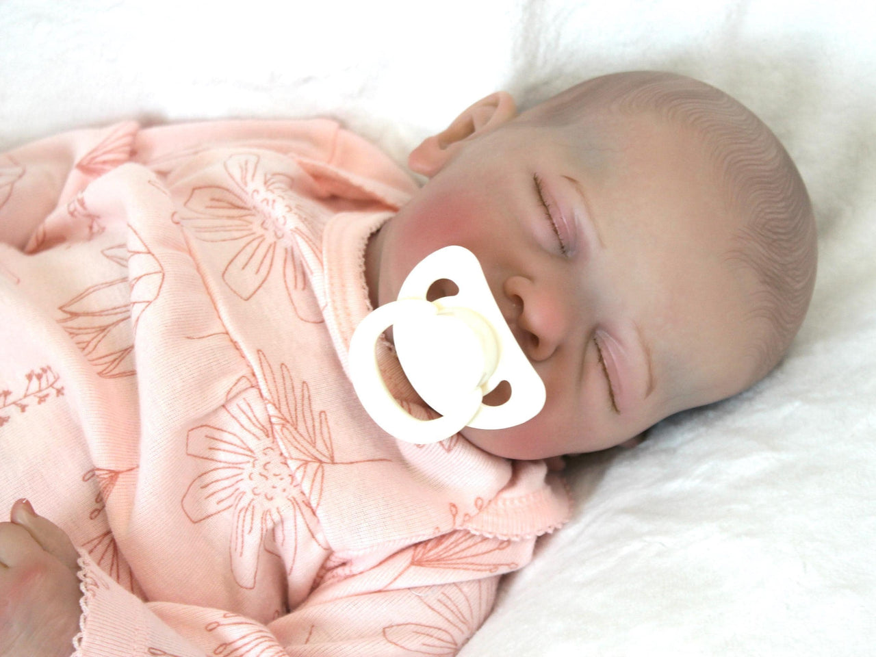 A peaceful newborn baby sleeps soundly in a soft pink outfit, surrounded by a cozy blanket.