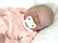 Thumbnail for A peaceful newborn baby sleeps soundly in a soft pink outfit, surrounded by a cozy blanket.