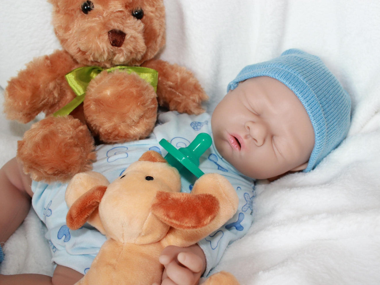 A baby doll wearing a blue hat is resting on a soft white blanket.