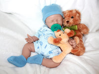 Thumbnail for A baby doll with a pacifier, accompanied by a soft stuffed animal, resting on a light-colored blanket.