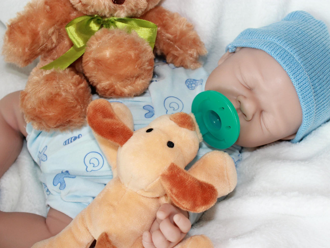 A baby doll with a pacifier, accompanied by a soft stuffed animal, resting on a light-colored blanket.