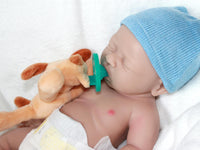 Thumbnail for A baby doll wearing a blue hat is resting on a soft white blanket.