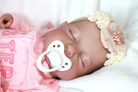 Thumbnail for A baby doll with a pacifier lies on a bed, highlighting its charming design and the peaceful setting.