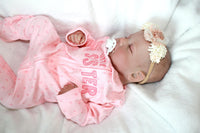 Thumbnail for A baby doll with a pacifier lies on a bed, highlighting its charming design and the peaceful setting.