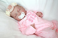 Thumbnail for A baby doll with a pacifier is positioned on a bed, emphasizing its adorable appearance and tranquil environment.