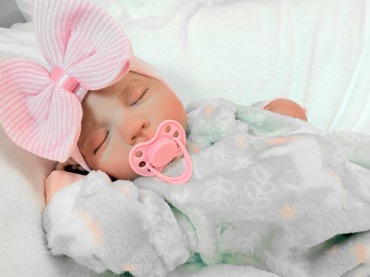 Newborn baby girl in a gray outfit with a pink bow, peacefully resting on a soft blanket.