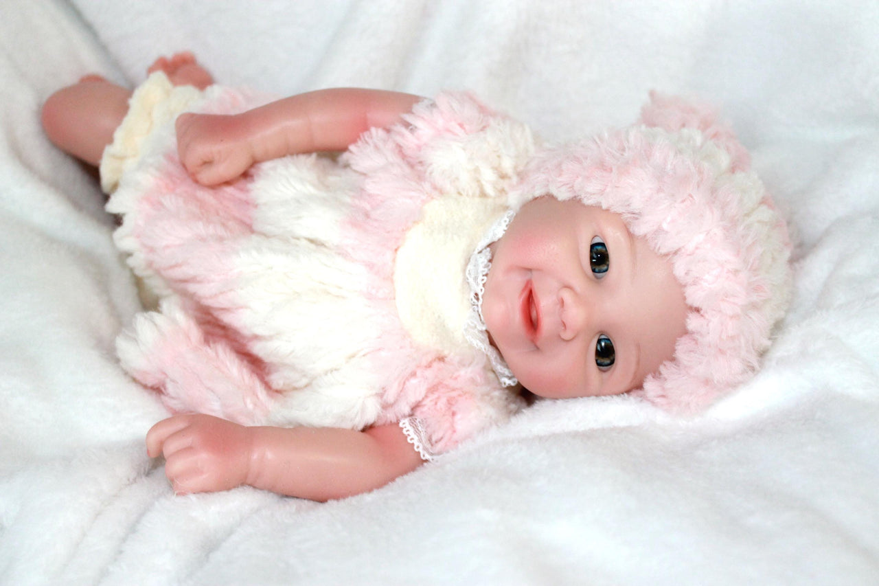 A cute baby doll wearing pink attire and a hat, positioned on a light background.