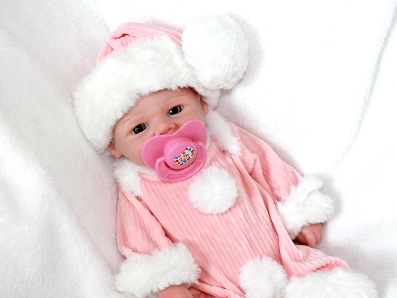 A baby doll with a pacifier rests on a soft blanket, showcasing its cute features and gentle expression.