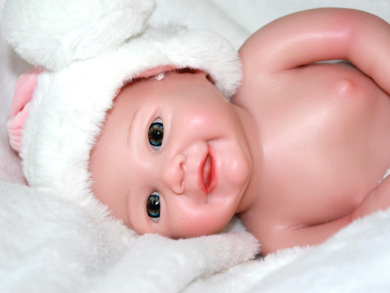 A baby doll wearing a pink and white outfit, featuring a sweet expression and soft, cuddly features.