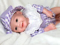Thumbnail for A baby doll dressed in a purple and white dress, featuring a sweet expression and soft, lifelike features.