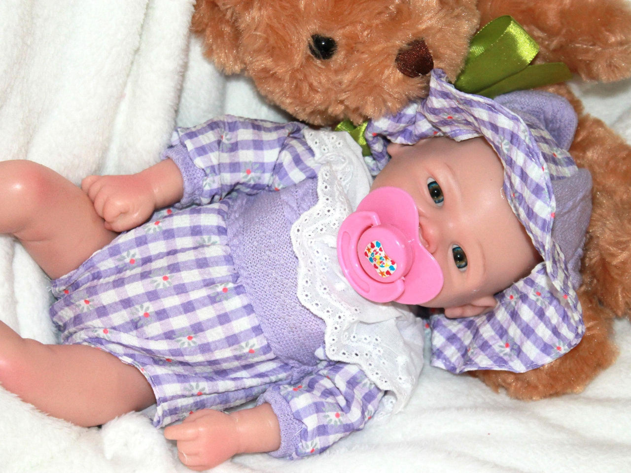 A teddy bear sits beside a doll, both positioned on a soft surface, creating a cozy playtime scene.