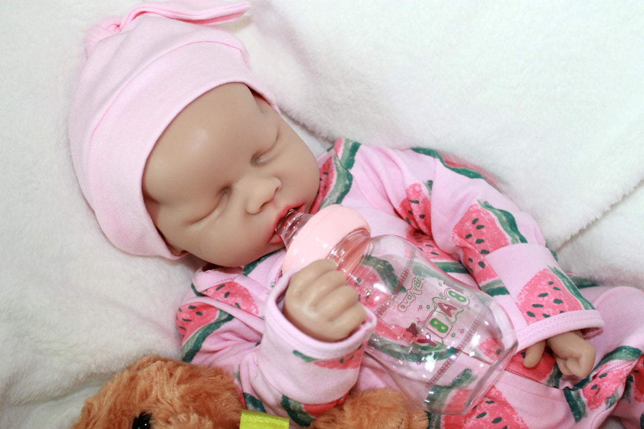 Infant doll lying on a blanket alongside a plush teddy bear.
