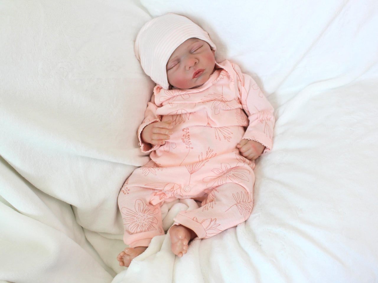 A baby doll positioned on a patterned blanket, emphasizing its cute appearance and soft texture.
