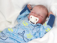 Thumbnail for A baby doll lying on a cozy blanket, highlighting its charming design and gentle expression.