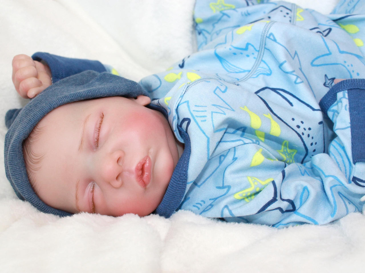 A baby doll resting on a soft blanket, showcasing its delicate features and clothing.