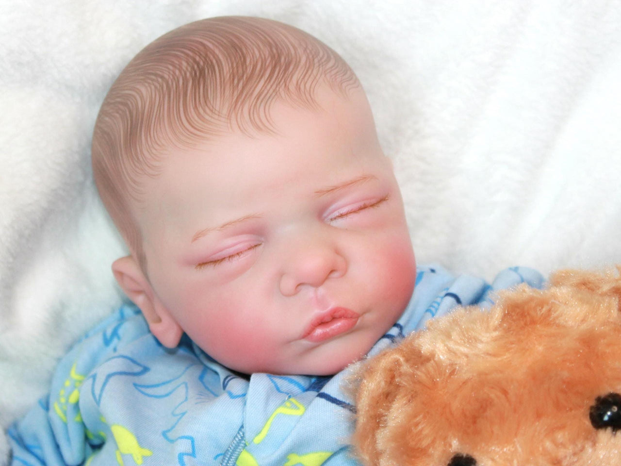 A baby doll lying on a cozy blanket, highlighting its charming design and gentle expression.