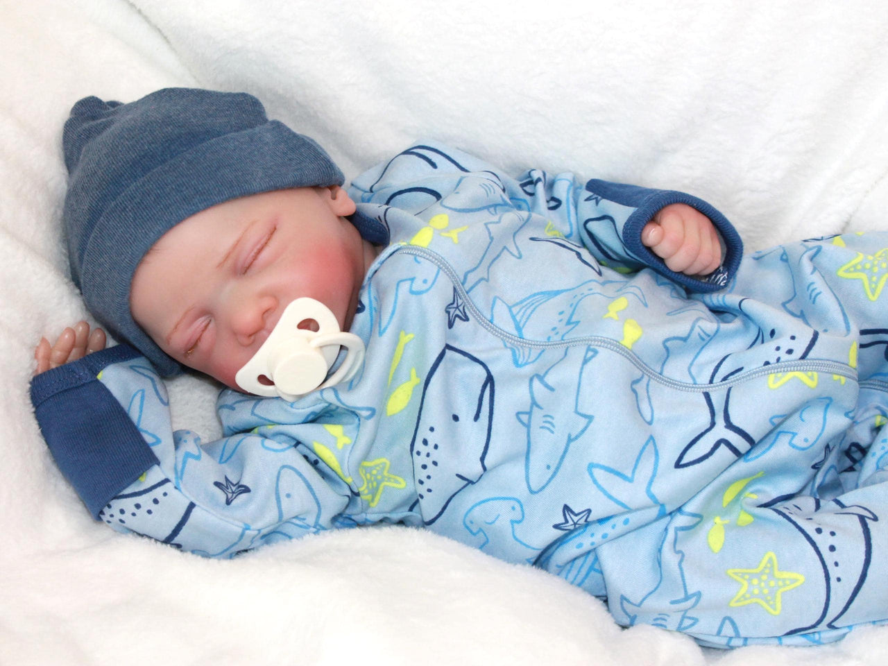 A baby doll positioned on a patterned blanket, emphasizing its cute appearance and soft texture.