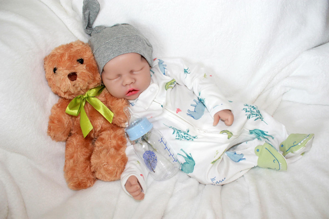 A baby doll positioned on a blanket, featuring a pacifier next to it.
