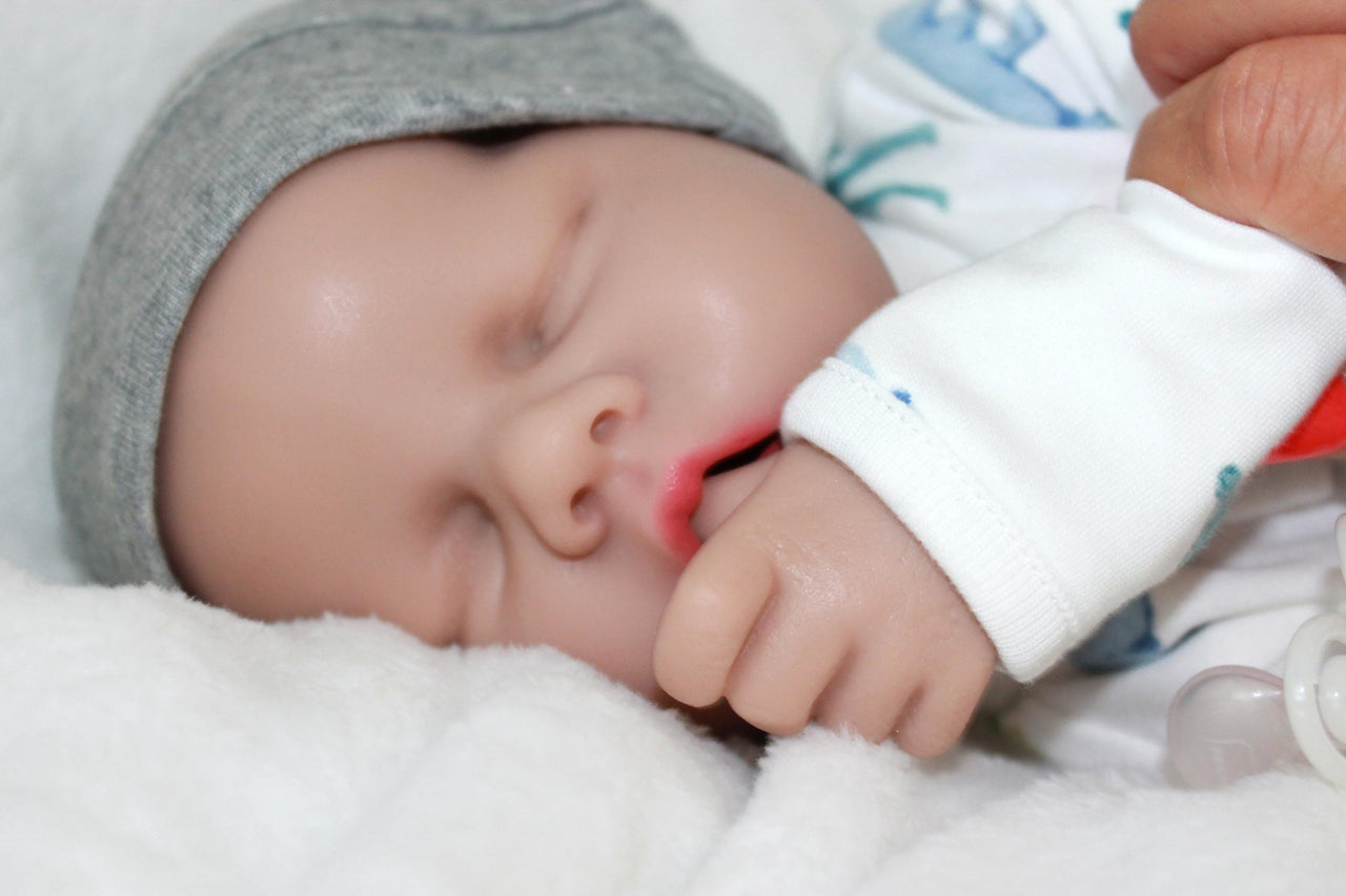 A baby doll positioned on a blanket, featuring a pacifier next to it.