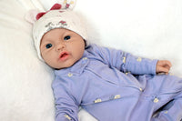 Thumbnail for A baby doll resting on a soft white blanket, showcasing its delicate features and clothing.