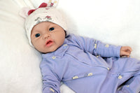 Thumbnail for A baby doll resting on a soft white blanket, showcasing its delicate features and clothing.