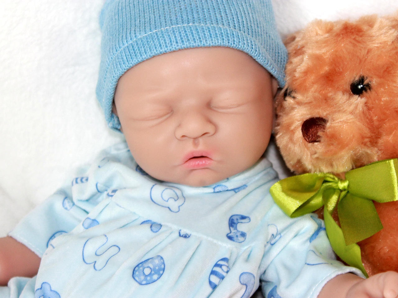 A baby doll with a pacifier, accompanied by a soft stuffed animal, resting on a light-colored blanket.