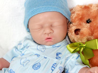 Thumbnail for A baby doll with a pacifier, accompanied by a soft stuffed animal, resting on a light-colored blanket.