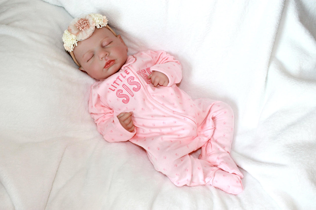 A baby doll resting on a neatly made bed, surrounded by soft blankets and pillows.