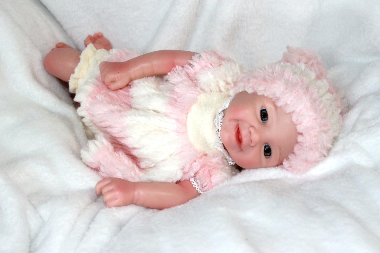 A cute baby doll wearing pink attire and a hat, positioned on a light background.