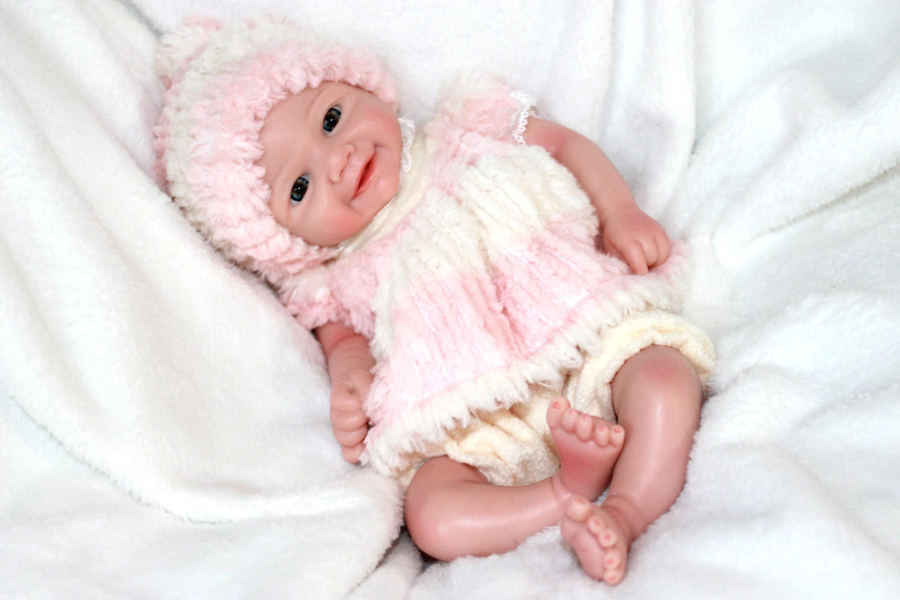 A cute baby doll wearing pink attire and a hat, positioned on a light background.