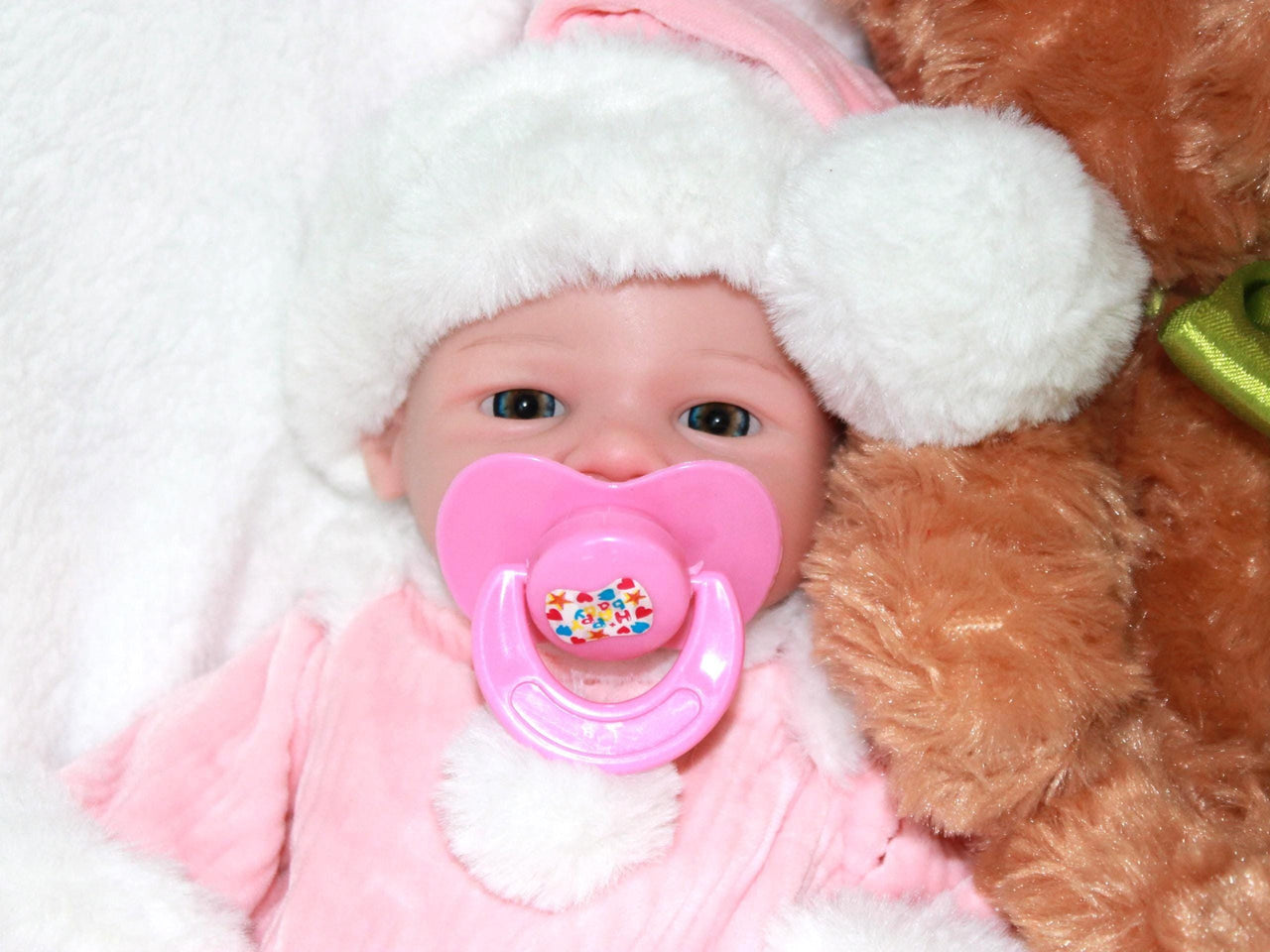 A baby doll with a pacifier rests on a soft blanket, showcasing its cute features and gentle expression.