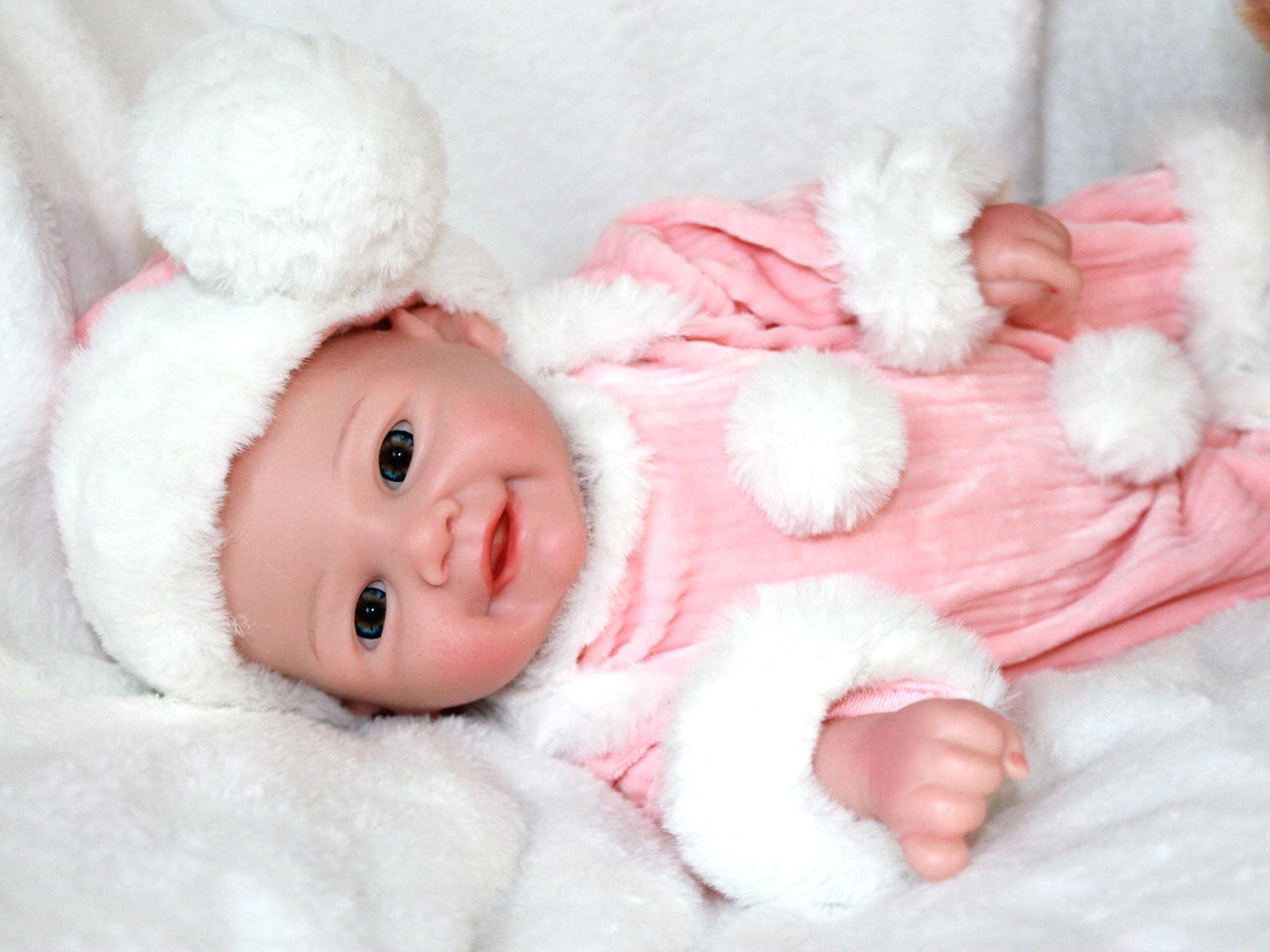A baby doll wearing a pink and white outfit, featuring a sweet expression and soft, cuddly features.