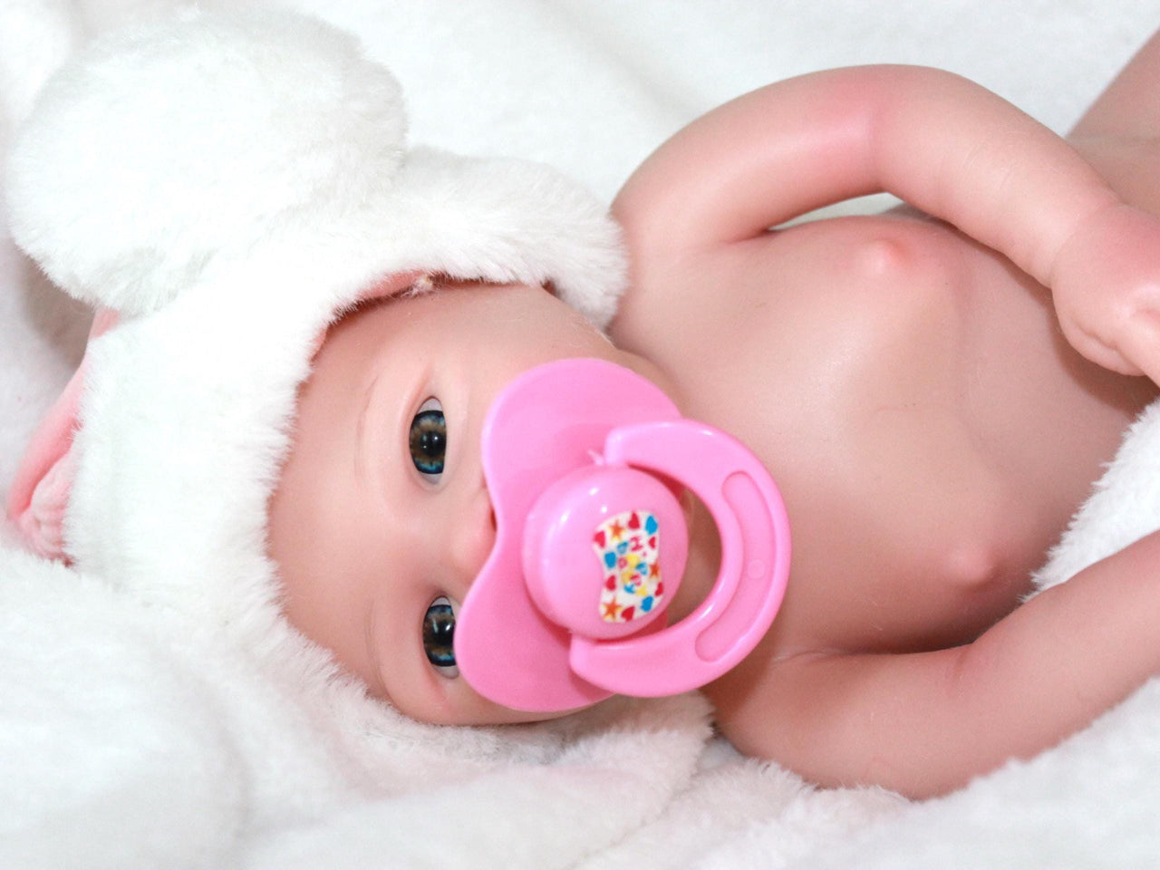 A baby doll with a pacifier rests on a soft blanket, showcasing its cute features and gentle expression.