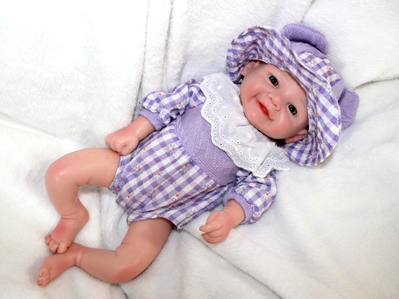 A baby doll dressed in a purple and white dress, featuring a sweet expression and soft, lifelike features.