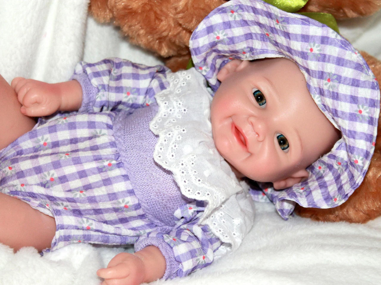 A baby doll wearing a charming purple and white dress, showcasing delicate details and a friendly smile.