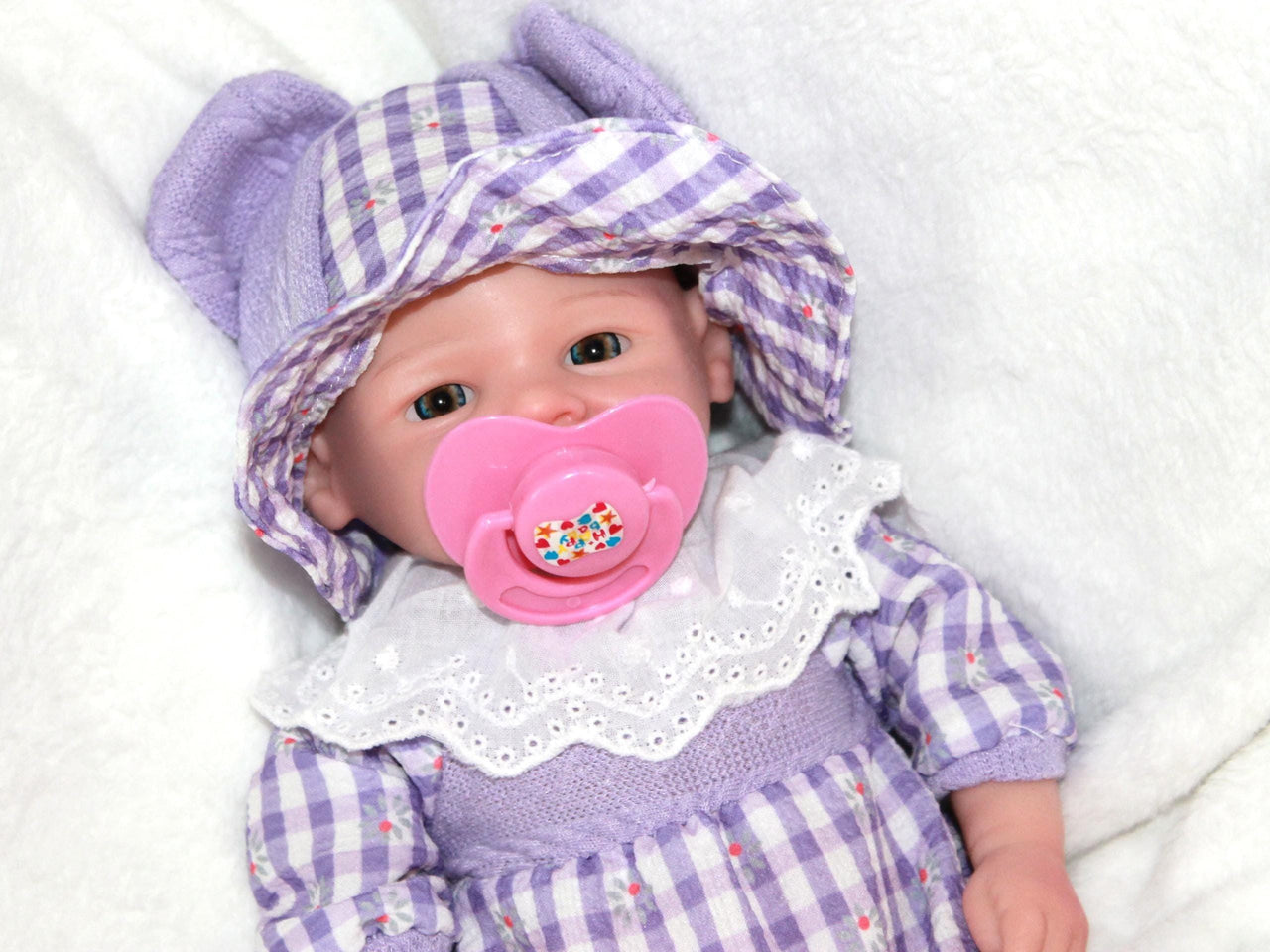 A baby doll wearing a charming purple and white dress, showcasing delicate details and a friendly smile.